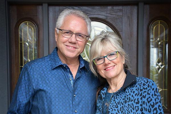 photo of Bill and Joann Truby in blue shirts standing in front of a door - Truby Achievements a leading source for leadership and management training