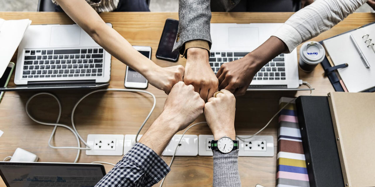 team fist bump while working - from Teamwork Synergy – Get More Done with Less article by Truby Achievements, leading provider of leadership training