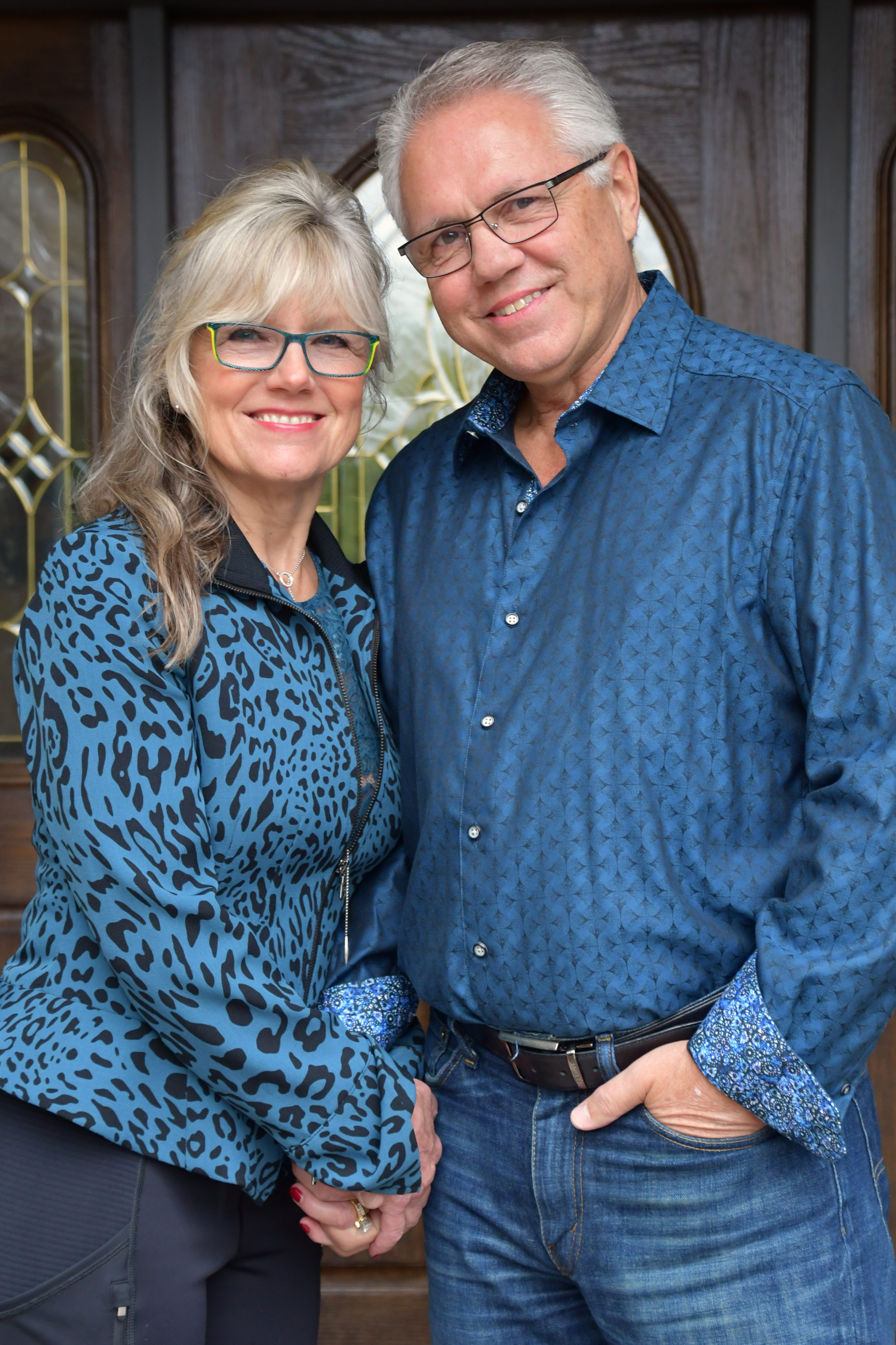 Oct2018c203 photo of Bill and Joann Truby in blue shirts standing in front of a door (larger view) - Truby Achievements a leading source for leadership and management training