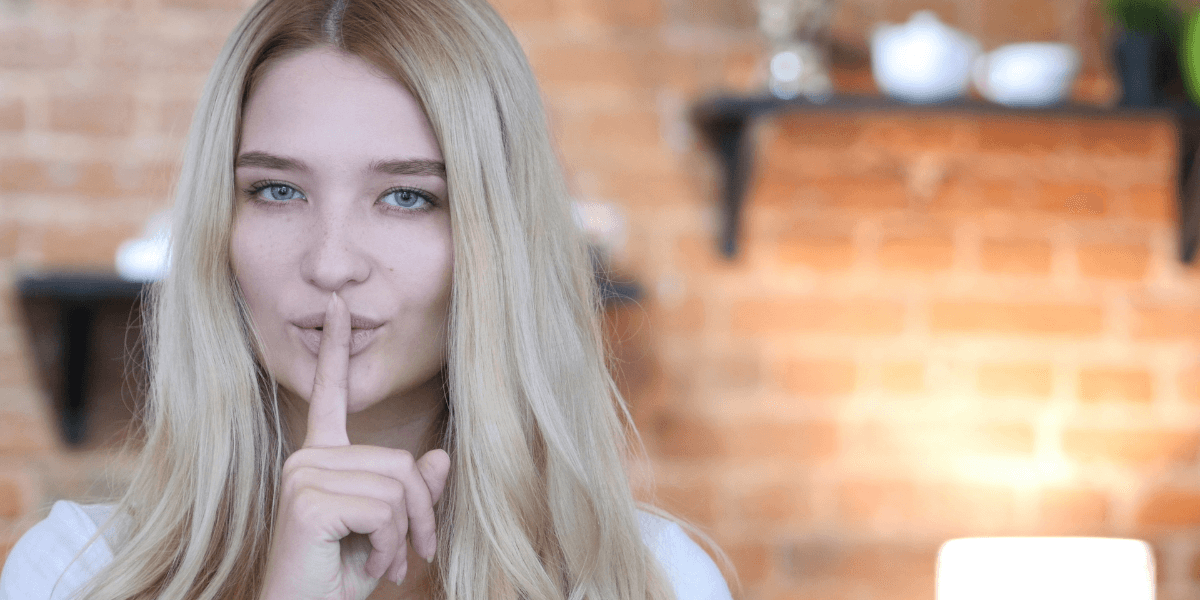 business woman holding her finger over her mouth for silence - featured image for business article from truby achievements - Improve Your Communications By Staying Silent