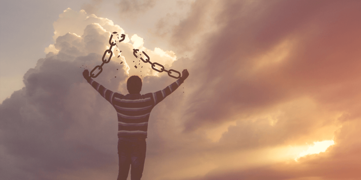 silhouette of a man breaking chains in front of sunset - achieve freedom blog post featured image