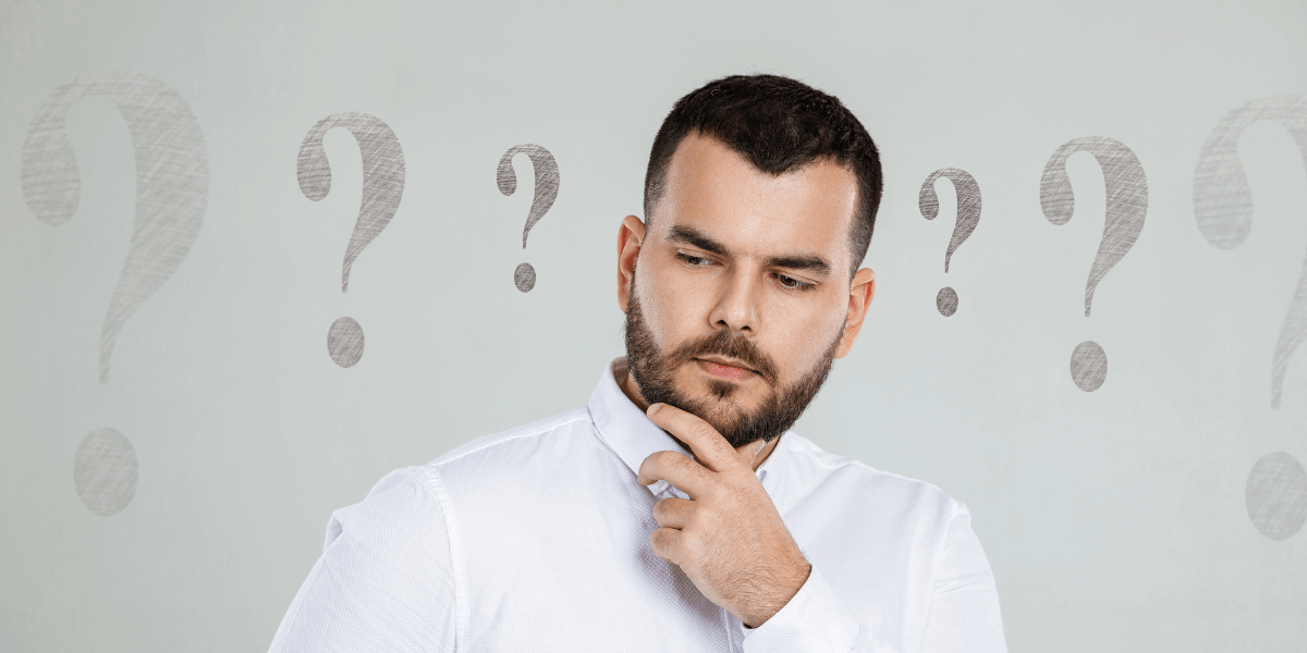 bearded man in white shirt holding his chin surrounded by question marks - featured image for asking better questions blog by truby achievements