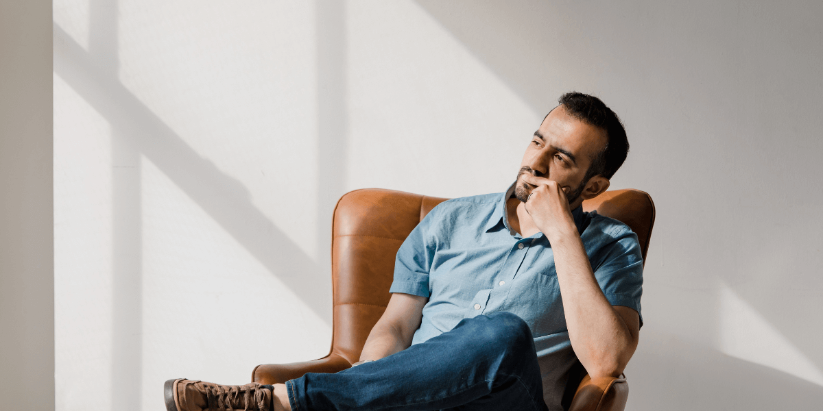 man in a blue shirt and jeans sitting in a leather chair thinking - possibility thinking versus probability thinking blog by truby achievements