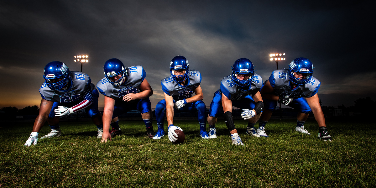 five football players at play line in teal uniforms with a dark stormy background - featured image for state of success blog by truby acheivements