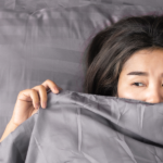 woman laying in bed with gray sheets and covering half her face - featured image for it's all in your head blog by truby achievements