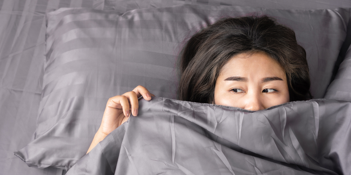 woman laying in bed with gray sheets and covering half her face - featured image for it's all in your head blog by truby achievements