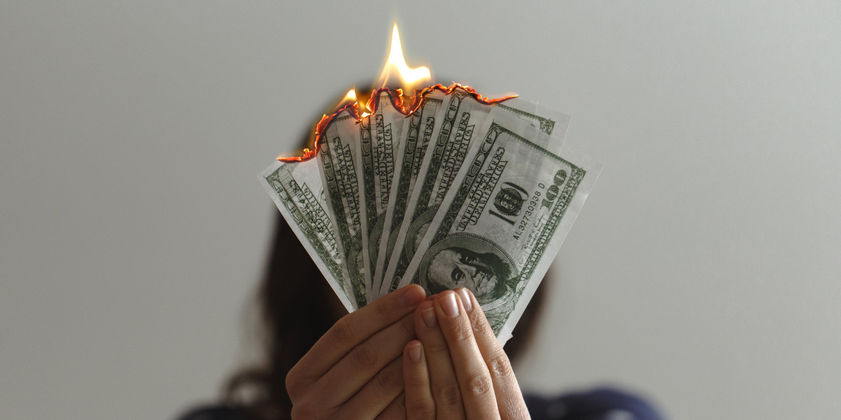 woman holding paper money in front of her face that is on fire - featured image for sunk cost effect blog by truby achievements