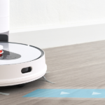 A white robotic vacuum cleaner docks itself at a charging station on a light wood floor, with a blue directional arrow path overlayed in front of it – featured image for Learning from Failure blog by Truby Achievements.