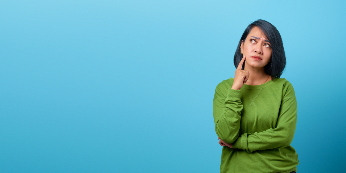 asian woman in green shirt holding her finger against her chin as she thinks with blue background - visualizing blog by truby achievements